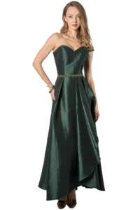 Woman in a dark green velvet strapless evening gown with a beaded belt, posing with one hand on hip and wearing gold jewelry.