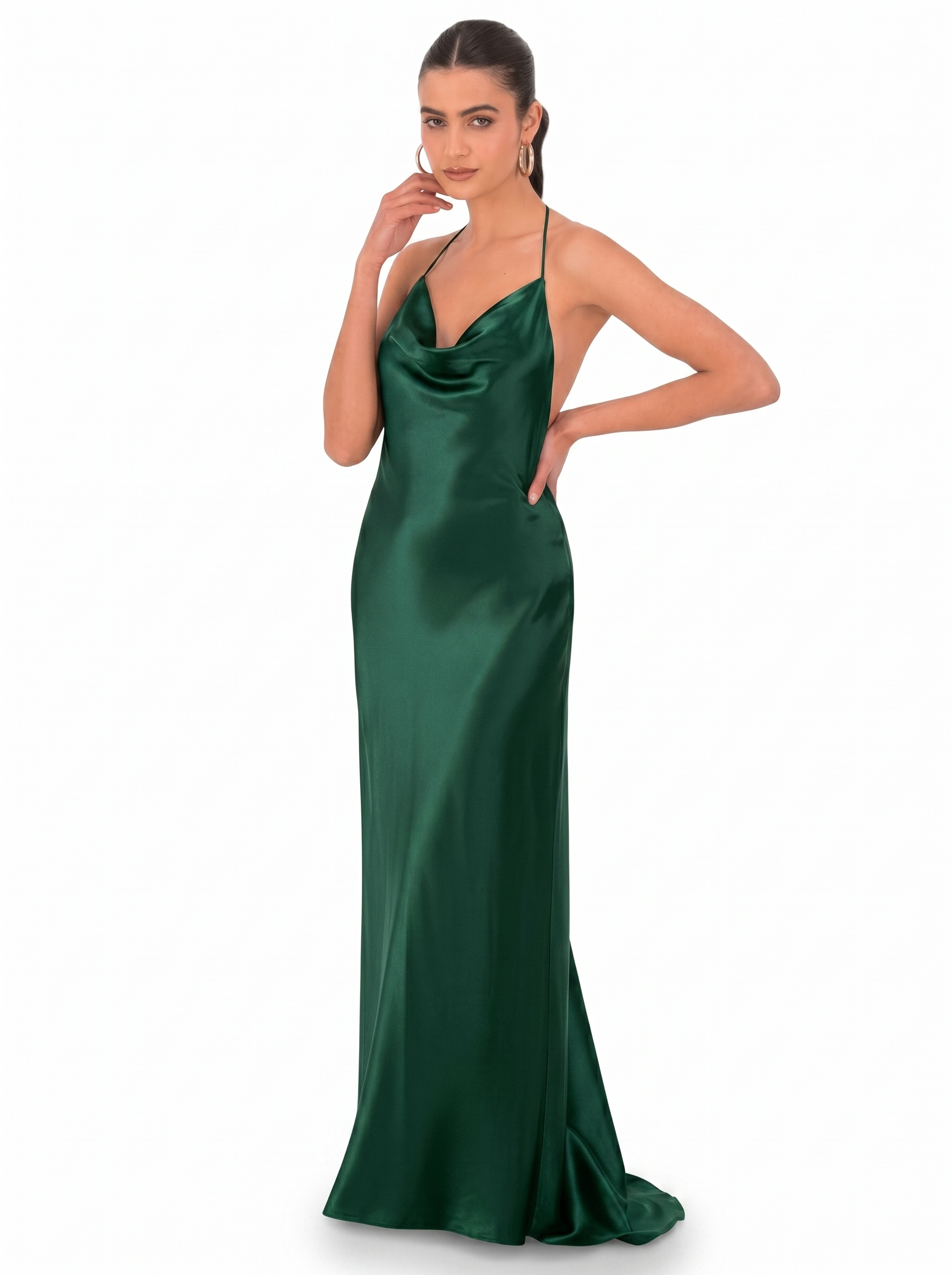 Woman in an emerald green satin halter gown, posed with one hand near her face and the other on her hip against a white backdrop.