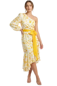 Woman in a white and yellow floral one-shoulder dress with a wide yellow sash, posing with hand on hip.