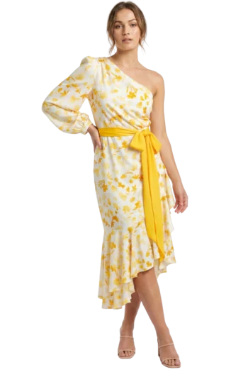 Woman in a white and yellow floral one-shoulder dress with a wide yellow sash, posing with hand on hip.