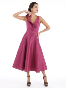 Woman modeling a magenta satin sleeveless midi dress with a ruffled V-neckline and fitted waist, wearing black strappy heels.