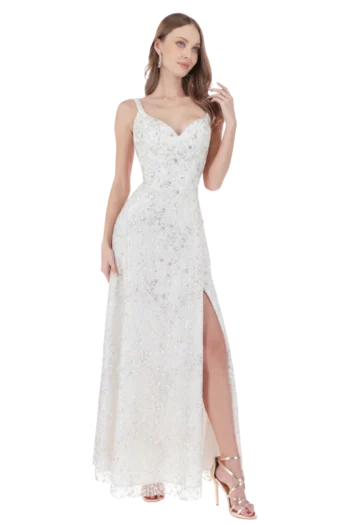 Woman in a white sequined evening gown with a thigh-high slit, wearing earrings and strappy heels, posing gracefully.