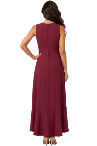 Back view of a woman in a burgundy sleeveless gown with a center back zipper and a long flowing skirt, one hand on her hip, with wavy hair cascading down.