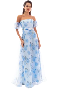 Woman in a light blue floral off-shoulder gown, standing and facing slightly left, with her hair pulled back and subtle jewelry.