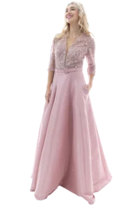 Woman in a pale pink lace blouse with a matching long pink skirt, smiling with one hand in a pocket.