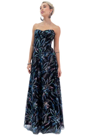 Woman wearing a strapless, maxi dress with a dark background and a colorful floral print, standing against a white background