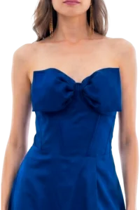 Woman wearing a blue strapless dress with a bow at the chest and long gold dangling earrings.