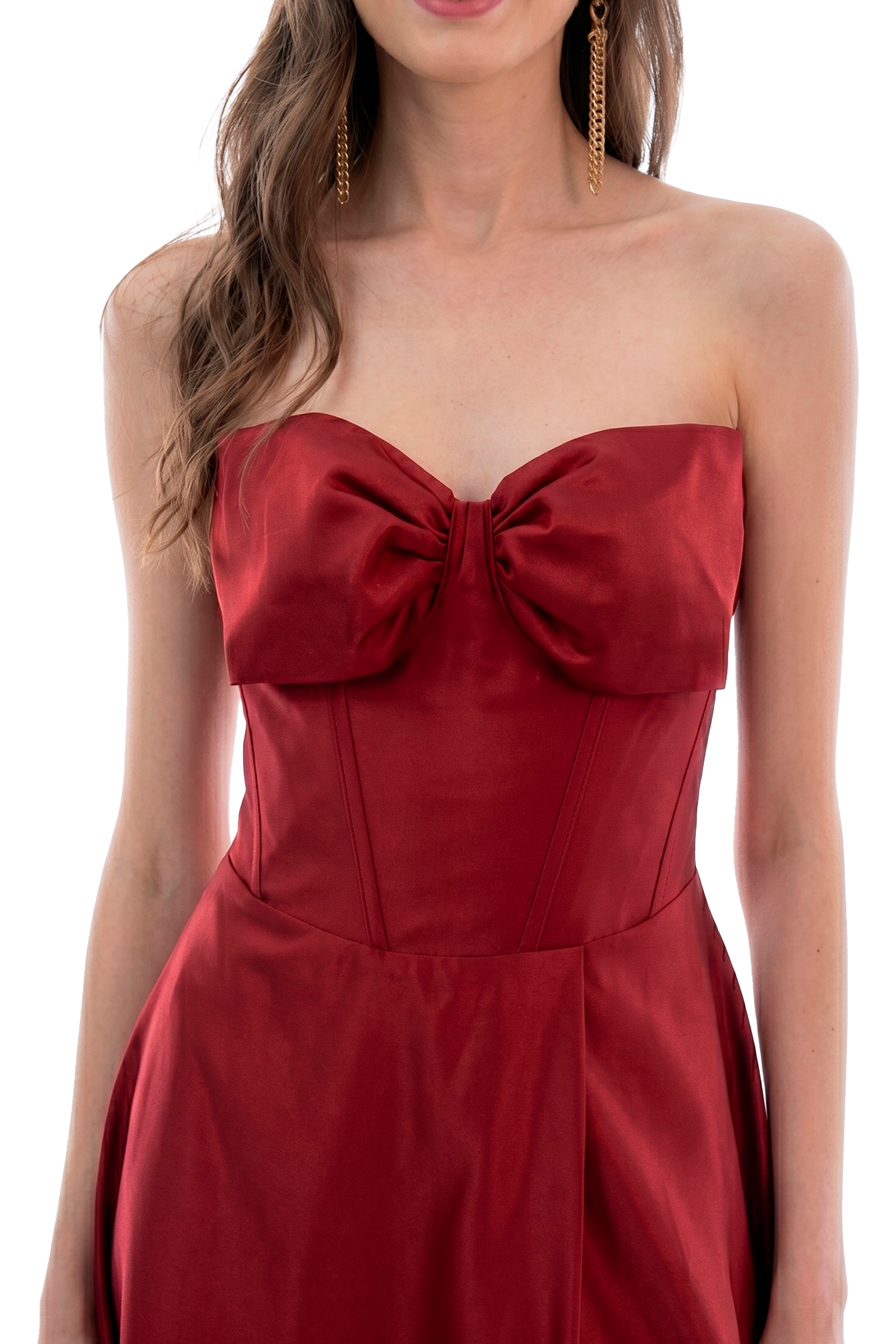 Woman wearing a red strapless satin dress with a large front bow and gold dangling earrings, single-portrait cutout against a dark background.