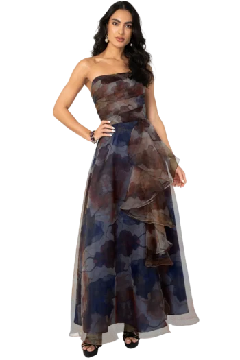 Woman modeling a strapless, layered sheer camo-print gown in blue, brown, and gray tones, hand on hip against a black backdrop.