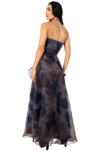 Woman in a strapless, floor-length floral gown, shown from the back with dark hair and pearl earrings, standing gracefully.