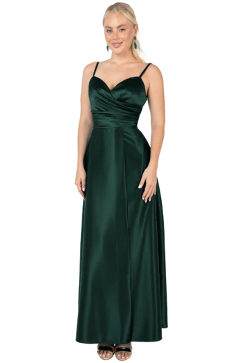 Full-length view of a woman in an emerald-green satin evening gown with thin straps, a draped bodice, and a long flowing skirt, standing with hands at her sides against a black background.