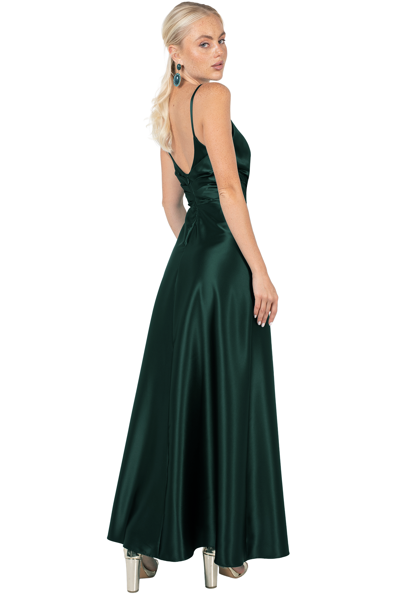 Woman wearing an emerald green satin evening gown seen from behind, open back and thin straps, with turquoise earrings.
