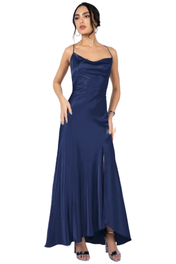 Woman in a navy satin evening gown with thin straps, standing with one hand on hip and wearing silver heels and jewelry.