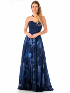 Model wearing a navy blue strapless evening gown with a pleated bodice and sheer, camo-patterned skirt, standing against a white background.