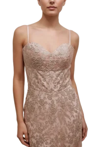 Woman wearing a blush pink lace evening gown with thin spaghetti straps and floral embroidery on the bodice and skirt.