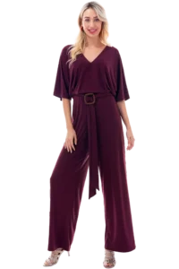 Woman wearing a burgundy jumpsuit with a wide-leg silhouette and a matching belt, standing against a black background.