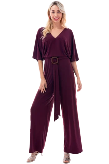 Woman wearing a burgundy jumpsuit with a wide-leg silhouette and a matching belt, standing against a black background.