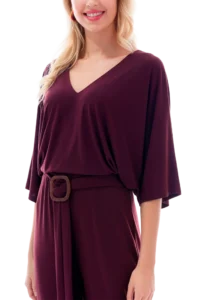Woman wearing a burgundy V-neck wrap-style jumpsuit with a square-buckle belt at the waist, from the shoulders to mid-thigh.