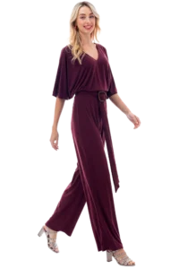 Woman wearing a burgundy jumpsuit with a belt walks forward, beige strappy heels visible.