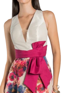 Close-up of a person wearing a white sleeveless V-neck top with a wide pink sash belt over a floral skirt.