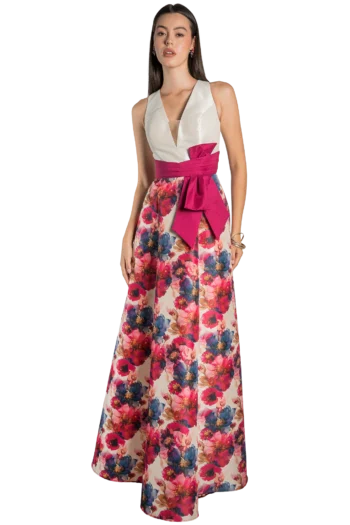 Woman wearing a white sleeveless V-neck top with a bright pink sash and a long floral skirt, posing against a black background.