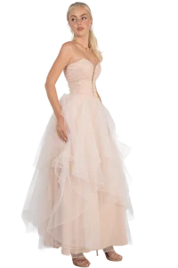 Woman in a blush pink strapless ball gown with a lace bodice and layered tulle skirt, wearing jewelry and sandals, posing to the side.