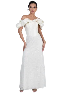 Full-length view of a woman wearing an ivory off-the-shoulder wedding gown with dramatic puff sleeves, intricate beaded lace, and open-toe heels, standing against a black background.