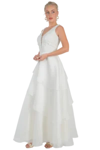 Bride in a white sleeveless wedding dress with a floral lace bodice and tiered, flowing skirt, standing in profile.