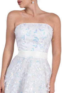 Close-up of a woman wearing a white strapless dress with blue and silver floral appliqués, showing shoulders and neckline, wearing a pearl earring.