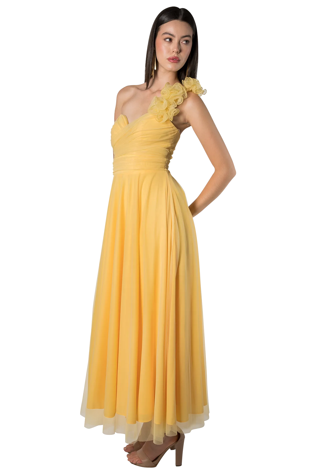 Full-body shot of a woman in a pale yellow, one-shoulder gown with a ruffled shoulder, standing with one hand on her hip.
