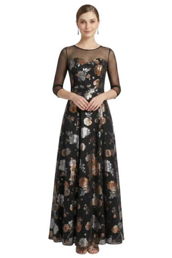Woman modeling a black floor-length floral gown with sheer mesh sleeves, hands gently clasped at waist.