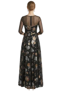 Back view of a woman in a black floral evening gown with sheer long sleeves and a low bun hairstyle