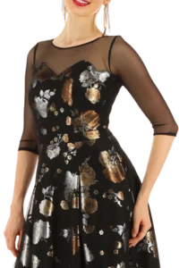 Woman wearing a black floral dress with sheer long sleeves, posing with hands at her sides.