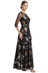 Woman in a long black floral gown with sheer three-quarter sleeves, posed in profile and smiling.