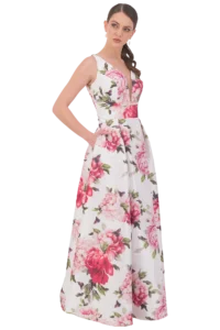 Model wearing a sleeveless white floral gown with large pink flowers, standing with one hand on the hip.