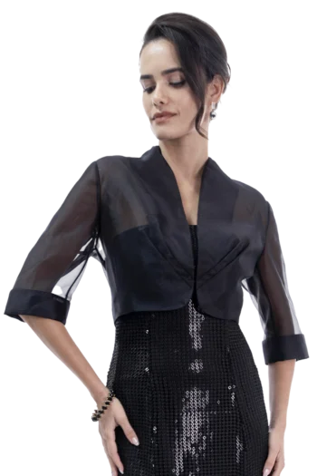 Woman in a sheer black jacket over a sequined black dress, facing left and looking down