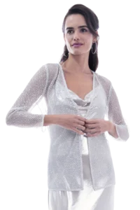 Woman in a glittering silver jacket and white dress, hands clasped, facing slightly to the side.