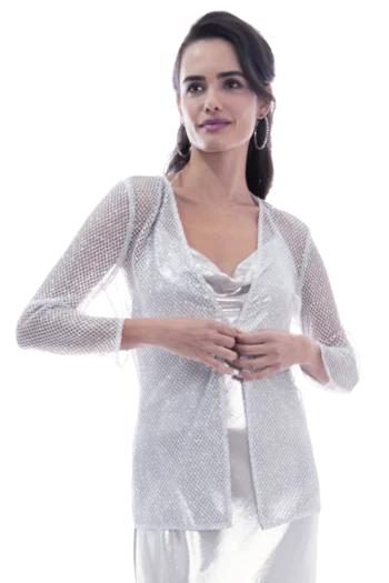 Woman in a glittering silver jacket and white dress, hands clasped, facing slightly to the side.