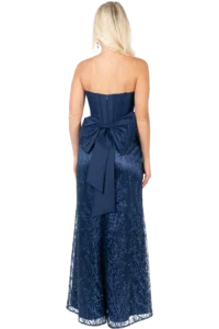 Back view of a woman in a navy strapless gown with a large bow at the waist and blue embroidery on the fabric.