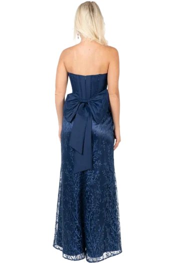 Back view of a woman in a navy strapless gown with a large bow at the waist and blue embroidery on the fabric.