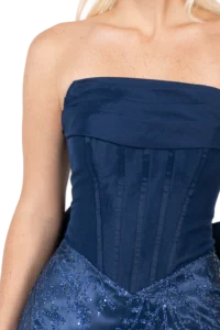 Close-up of a woman wearing a navy blue strapless gown with a pleated bodice and bead-embellished skirt. Freckled shoulders are visible.