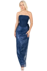 Full-length view of a woman in a strapless navy blue formal gown with a sequined, embroidered skirt, standing against a black background.