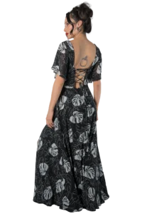 Woman in a black backless dress with white leaf pattern, facing left; lace-up back detail visible and a tattoo on her upper back.
