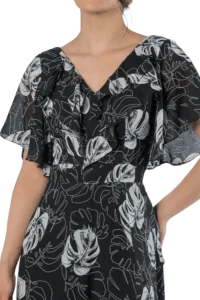 Woman wearing a black dress with a white abstract leaf print and a ruffled V-neck front.