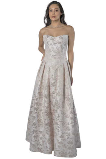 Woman in a strapless ivory lace gown with floral embroidery, standing against a plain background, wearing a necklace.