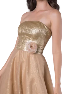 Close-up of a woman’s torso in a gold metallic strapless dress with a soft pink flower at the waist.] реальные