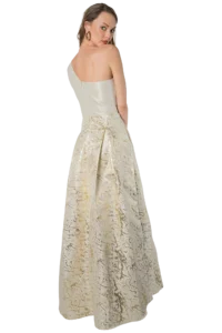 Model wearing a cream strapless gown with a gold textured brocade skirt, turned slightly toward the camera from the back area.
