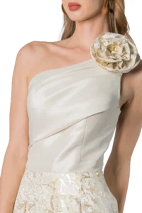 Woman in a white satin one-shoulder dress with a large fabric rose on the shoulder.