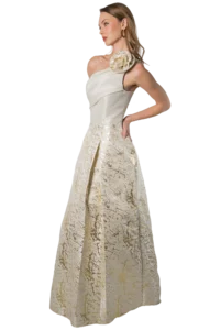 Profile view of a woman in an ivory gown with a large floral shoulder detail and gold skirt texture.