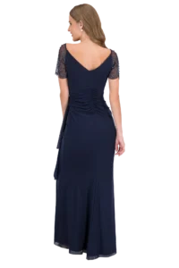 Back view of a woman in a navy evening gown with sheer, beaded sleeves and a ruched back detail.